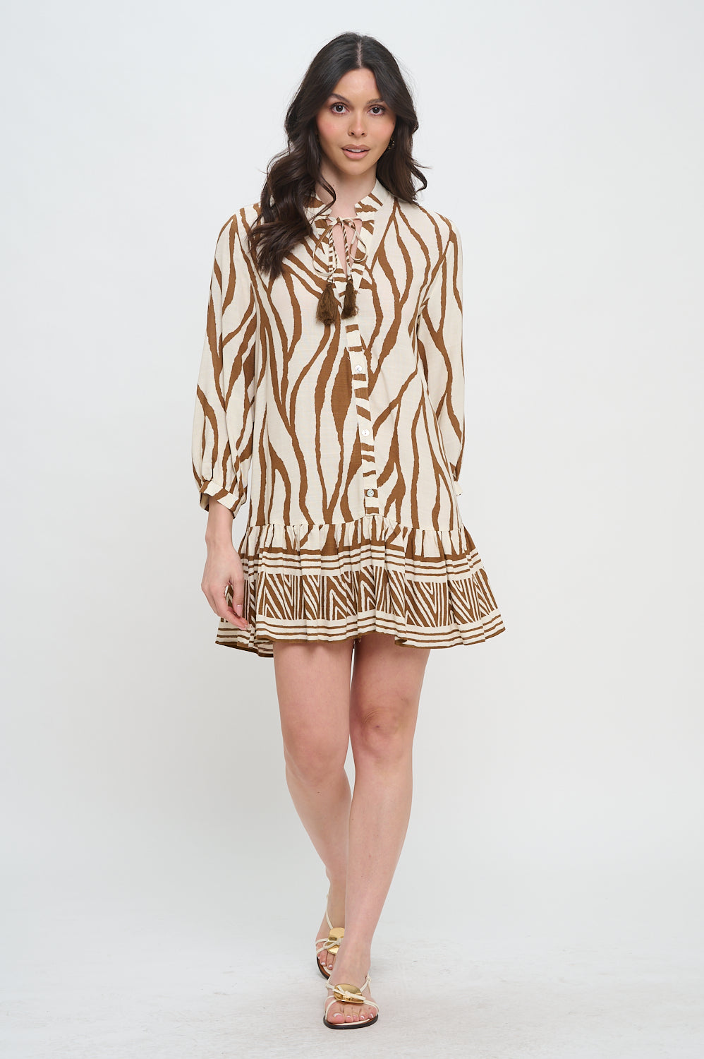 Woman wearing a long sleeve cotton short dress with tie neck, zebra-inspired print, and geometric border detailing at the hem.