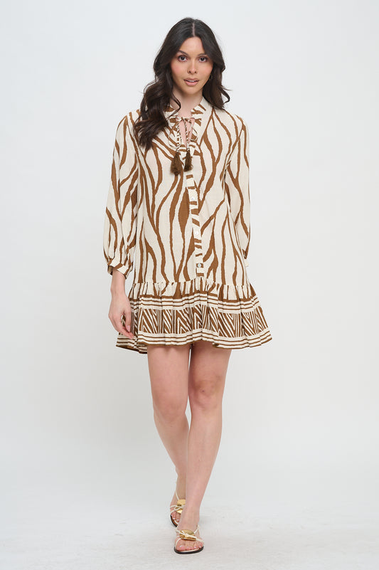 Woman wearing a long sleeve cotton short dress with tie neck, zebra-inspired print, and geometric border detailing at the hem.