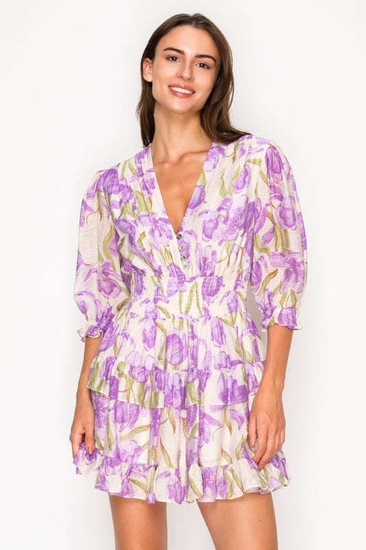 Model wearing the Aphrodites Garden Short Dress, a purple floral print mini dress with a V-neck and puff sleeves.