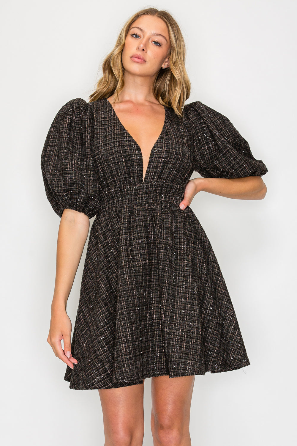 Model wearing the Ebony Tweed Puff Sleeve Dress, a black tweed mini dress with a deep V-neck, voluminous puff sleeves, and a smocked waist.