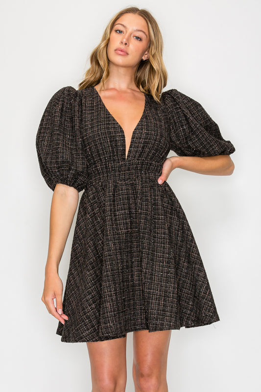 Model wearing the Ebony Tweed Puff Sleeve Dress, a black tweed mini dress with a deep V-neck, voluminous puff sleeves, and a smocked waist.