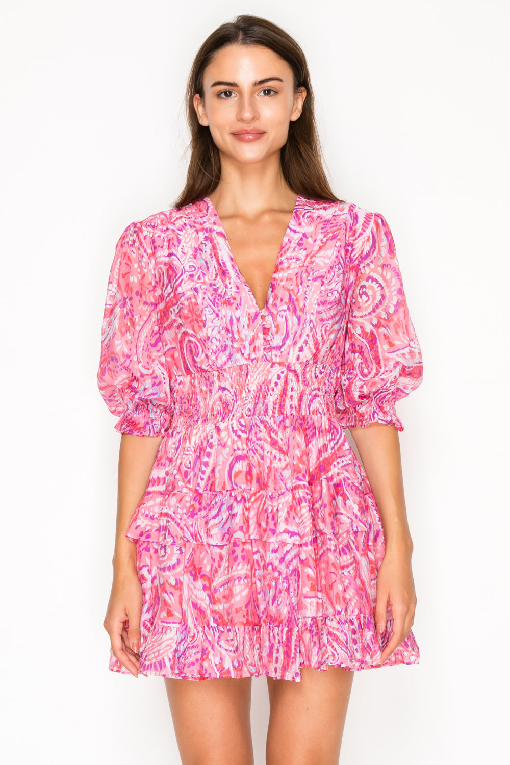 Model wearing the Rosey Echoes Short Dress, a vibrant pink and magenta paisley mini dress with a V-neck, puff sleeves, and a smocked waist.