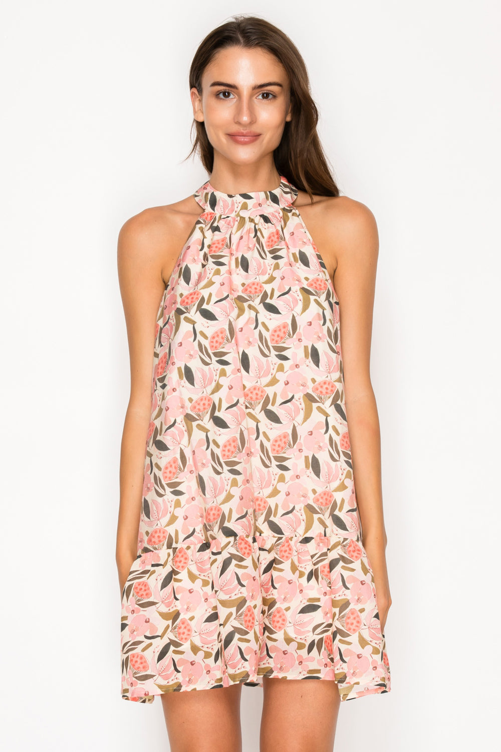 Model wearing the Peony Glow Halter Dress, a pink floral print mini dress with a high halter neck and a tiered hem.