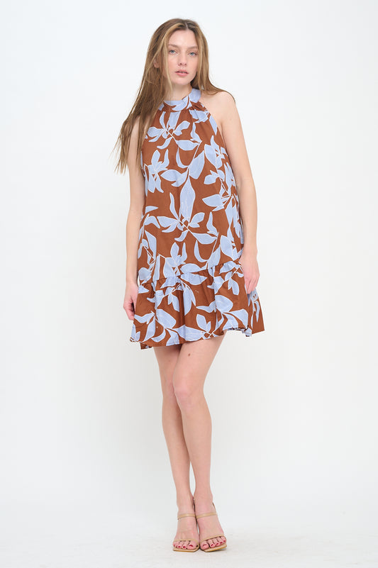 Woman wearing a sleeveless mini dress with a halter neckline and a brown-and-blue botanical print, featuring a relaxed fit and ruffled hem.