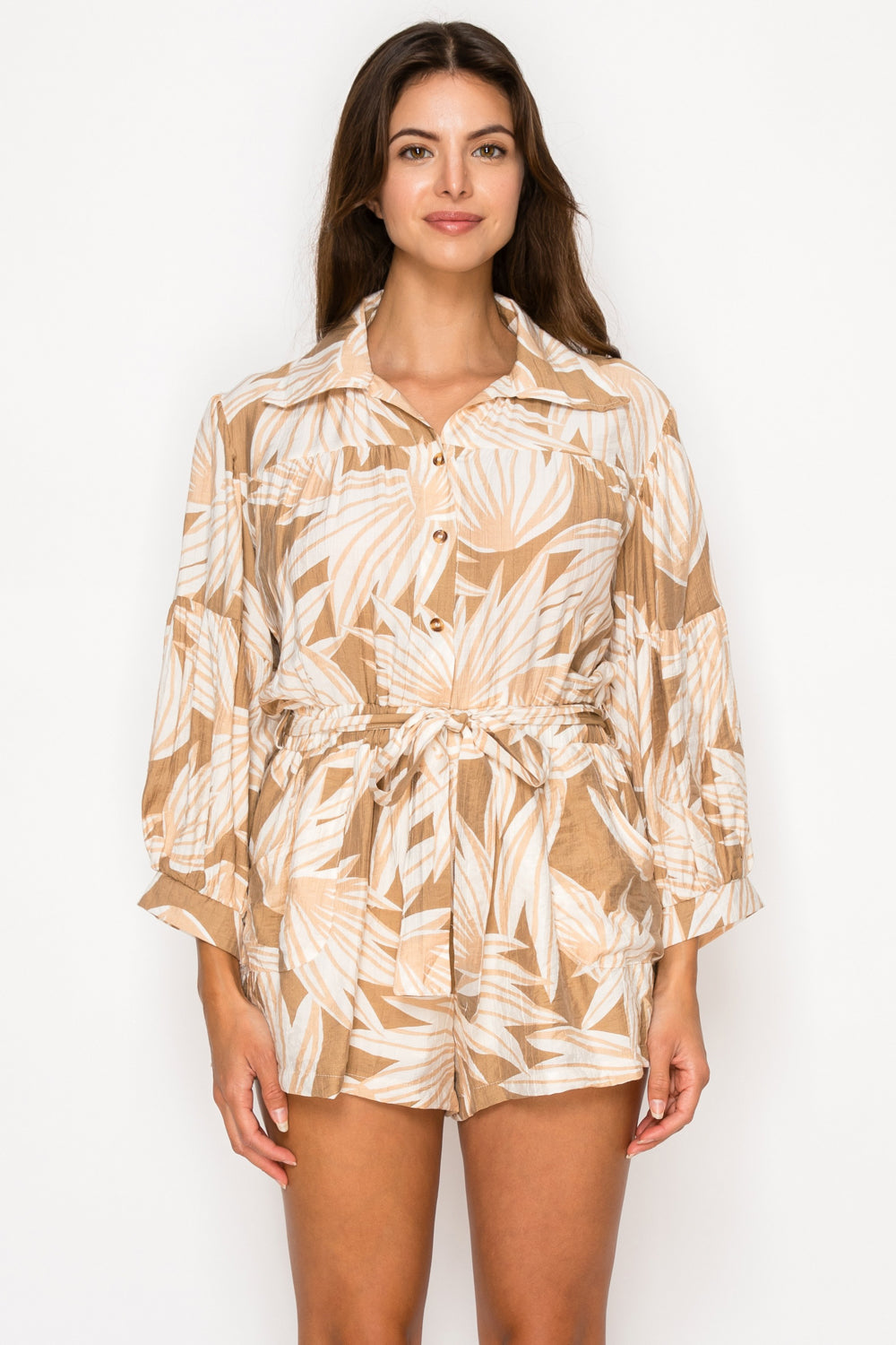 Model wearing the Eos Drift Romper, a tan and cream leaf print romper with a collar, long bishop sleeves, and a tie-waist.