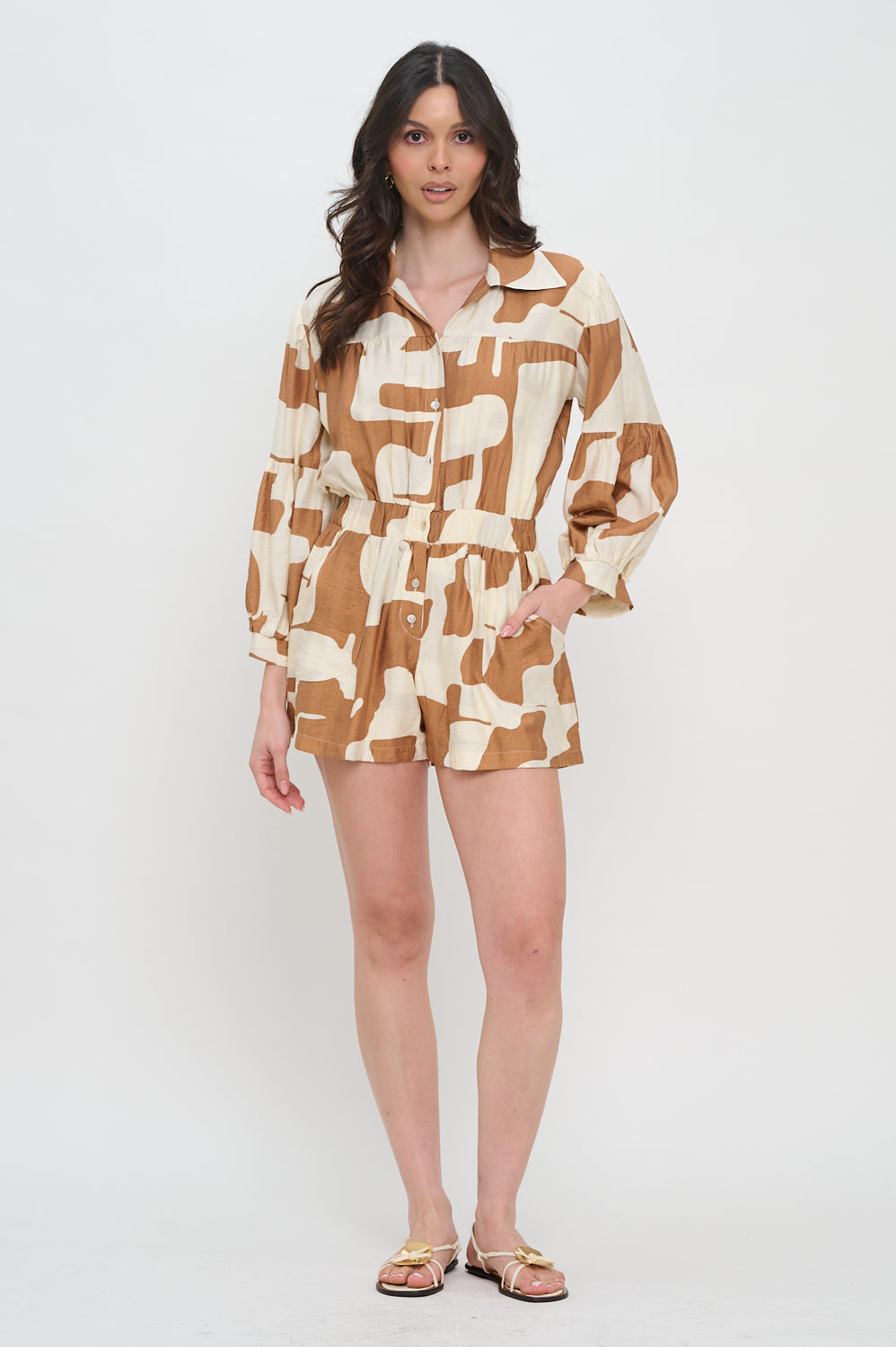 Woman wearing a long sleeve button-down romper with collared neckline, terracotta and cream abstract print, and elastic waist.