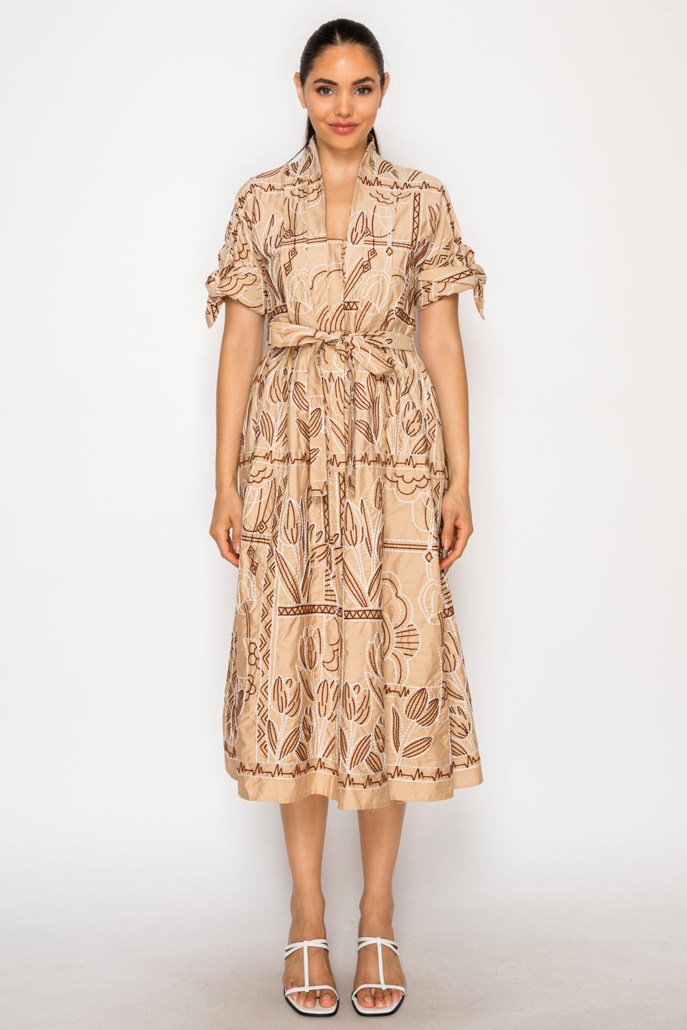 Model wearing the Myra Stitch Shirt Midi Dress, a tan embroidered dress with a collared V-neck, tie-waist, and tie-sleeve details.