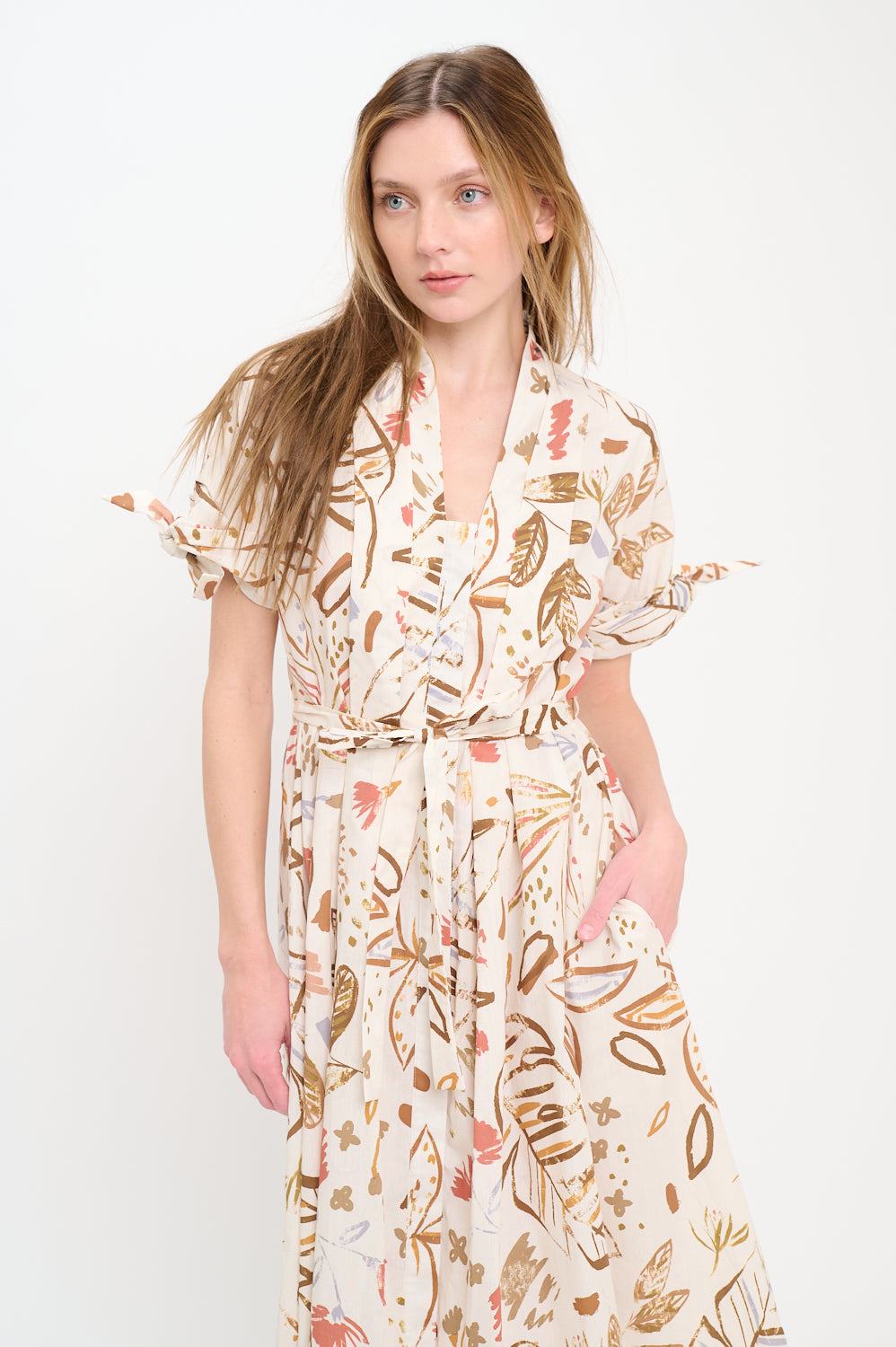 Woman wearing a collared button-front midi shirt dress with a botanical print in earthy tones, tie sleeves, and waist belt.