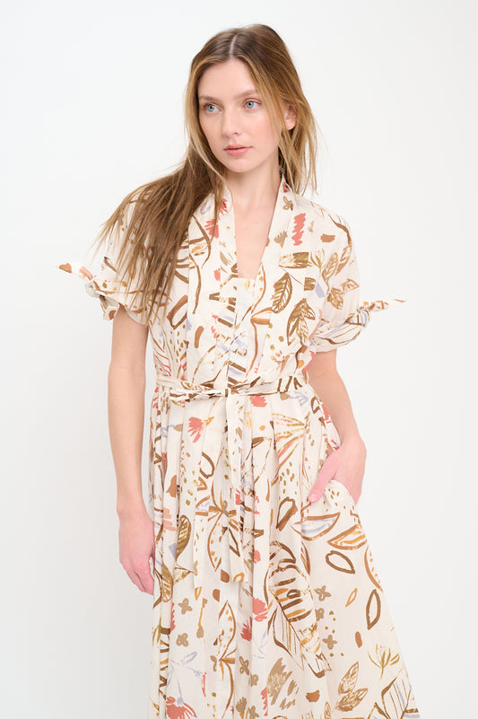 Woman wearing a collared button-front midi shirt dress with a botanical print in earthy tones, tie sleeves, and waist belt.