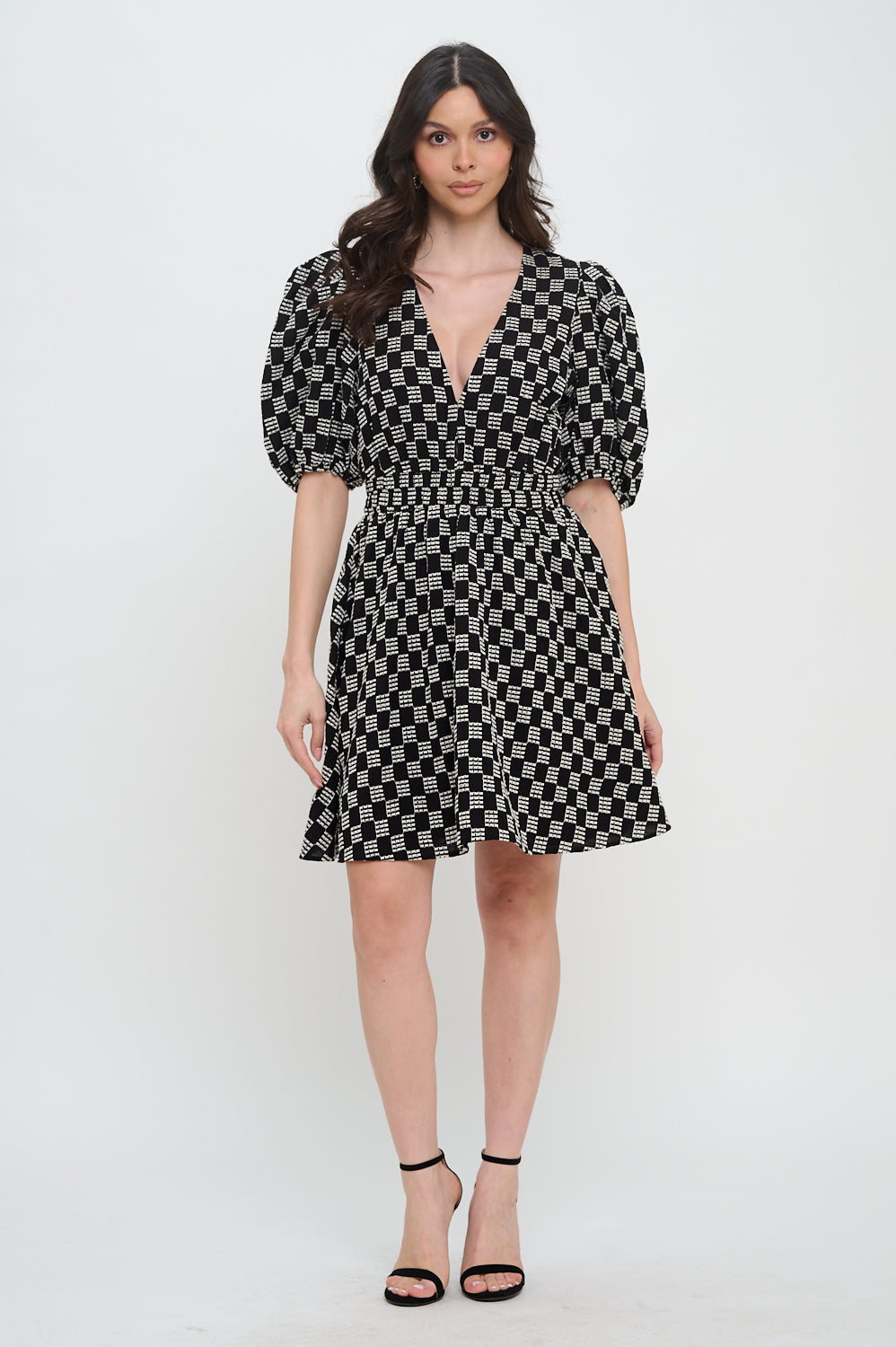 Model wearing the Midnight Weave Short Sleeve Dress from Meet Me in Santorini, a black and white checkerboard mini dress with a V-neck and puff sleeves.
