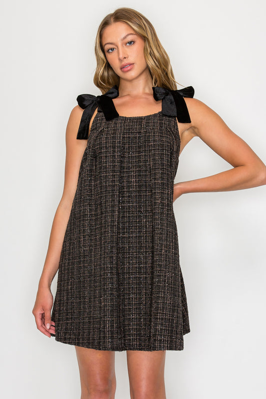 Model wearing the Ebony Tweed Tie Shoulder Dress, a black tweed mini dress with a square neckline and black velvet bows at the shoulders.