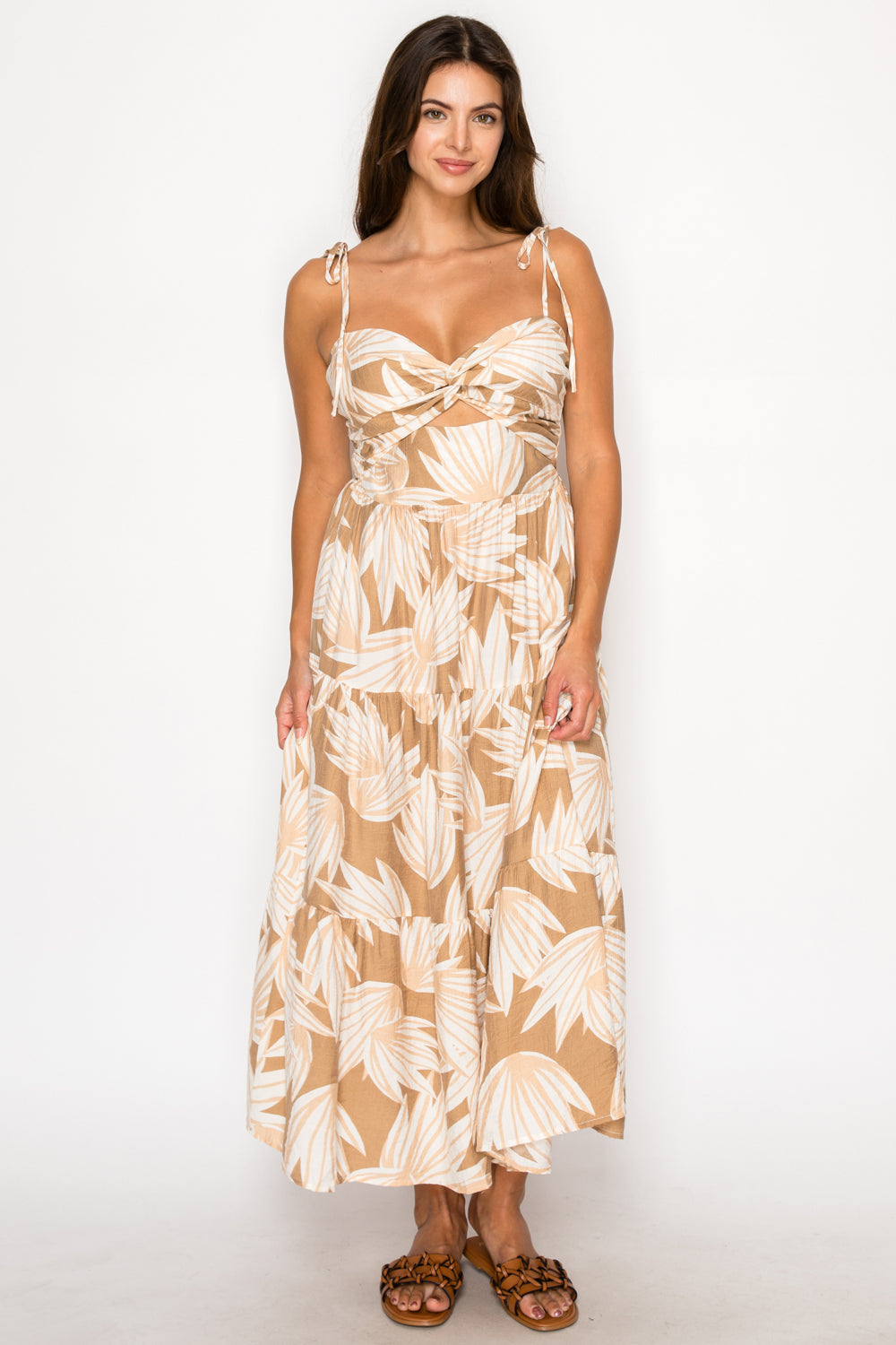 Model wearing the Eos Drift Maxi Dress, a tan and cream leaf print dress with tie-shoulders, a twist-front bust, and a tiered skirt.