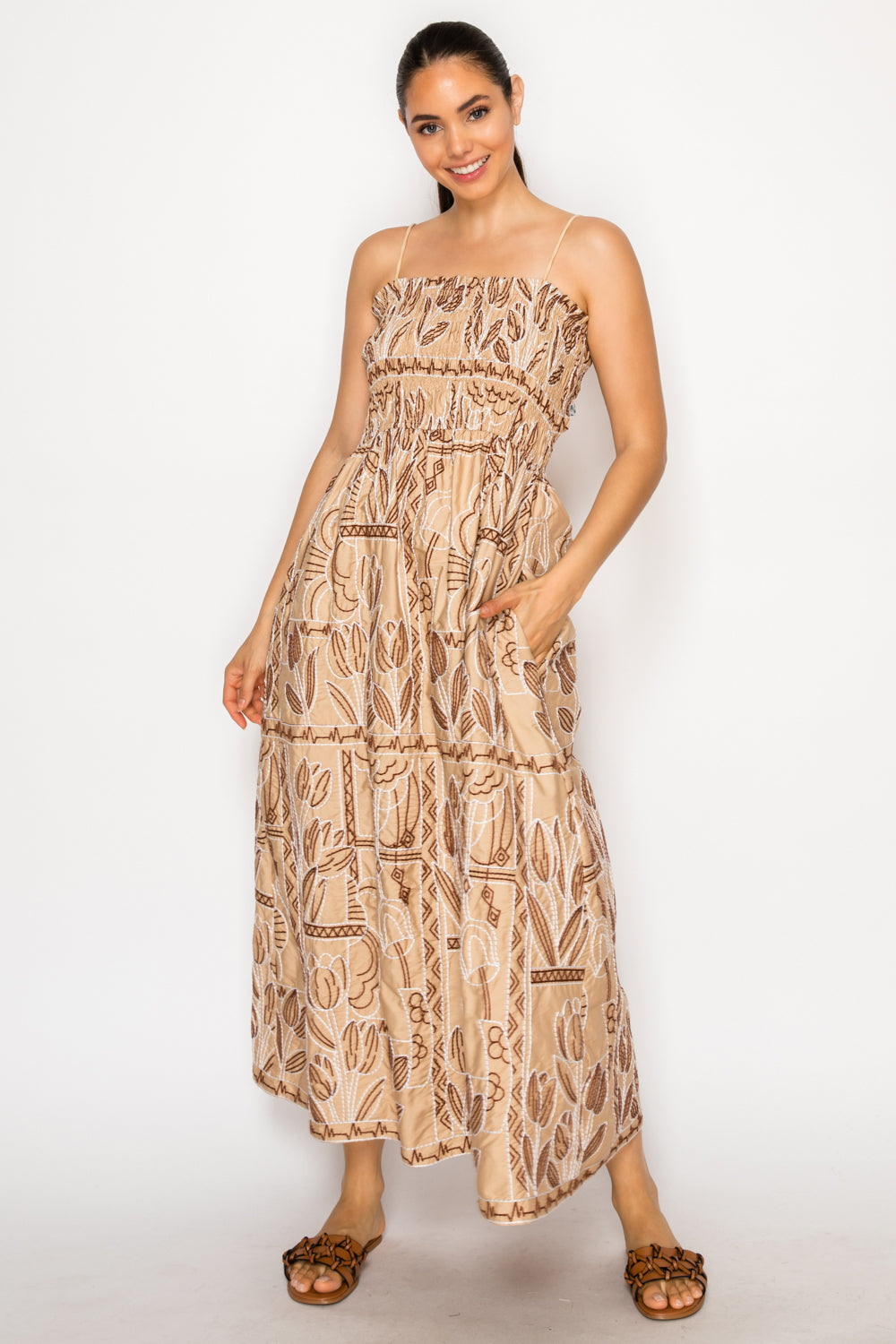 Model wearing the Myra Stitch Maxi Dress, a tan embroidered dress with a smocked bodice, spaghetti straps, and a tiered skirt.