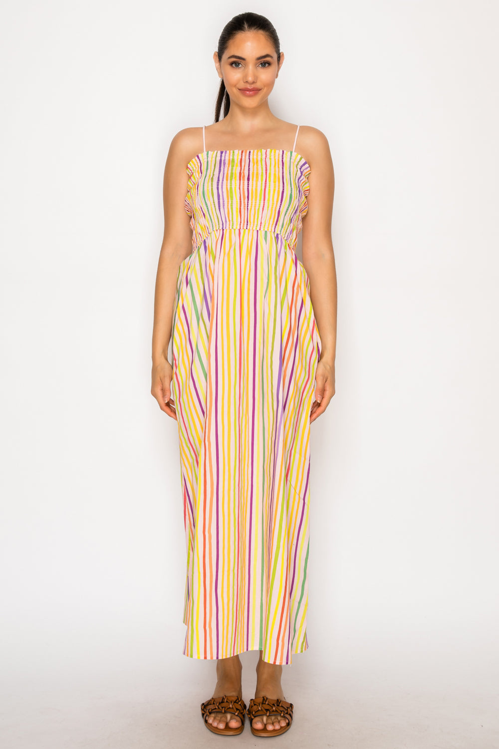 Model wearing the Paralia Stripes Midi Dress, a multi-colored vertical striped maxi dress with a smocked bodice and thin adjustable straps.