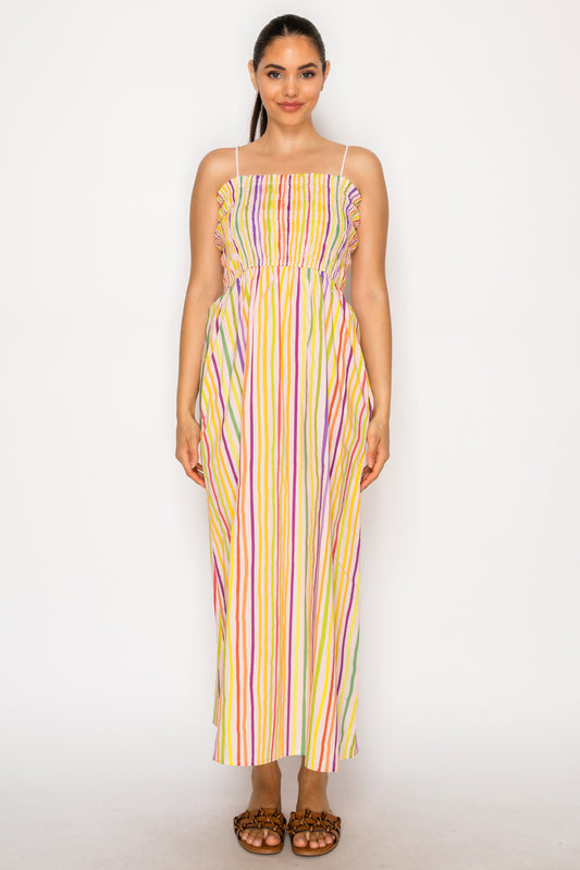 Model wearing the Paralia Stripes Midi Dress, a multi-colored vertical striped maxi dress with a smocked bodice and thin adjustable straps.