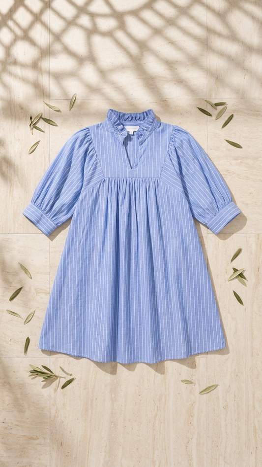 Flat lay of the Nautical Stripe Short Dress, a light blue and white pinstripe babydoll dress featuring puff sleeves and a ruffled collar on a stone tile background.