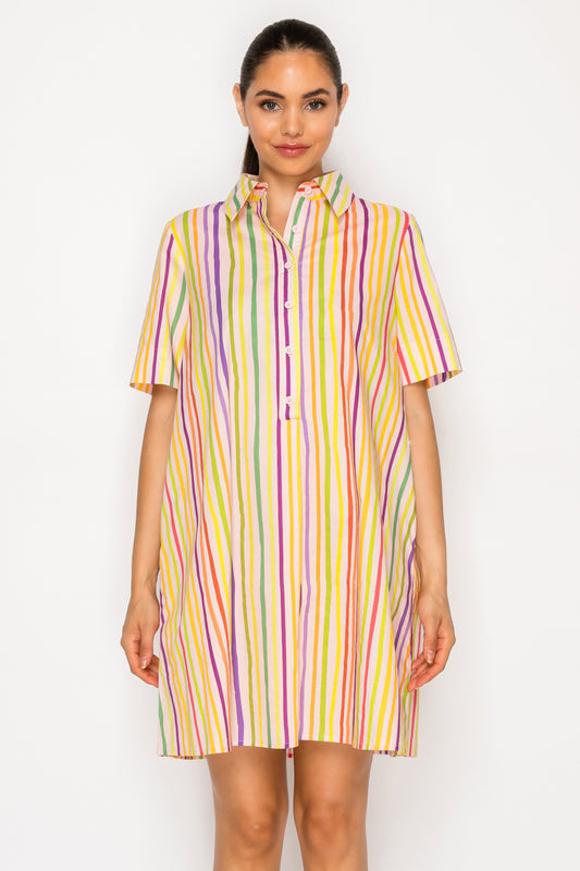 Model wearing the Paralia Stripes Shirt Dress, a multi-colored vertical striped mini dress with a collar, short sleeves, and an oversized fit.