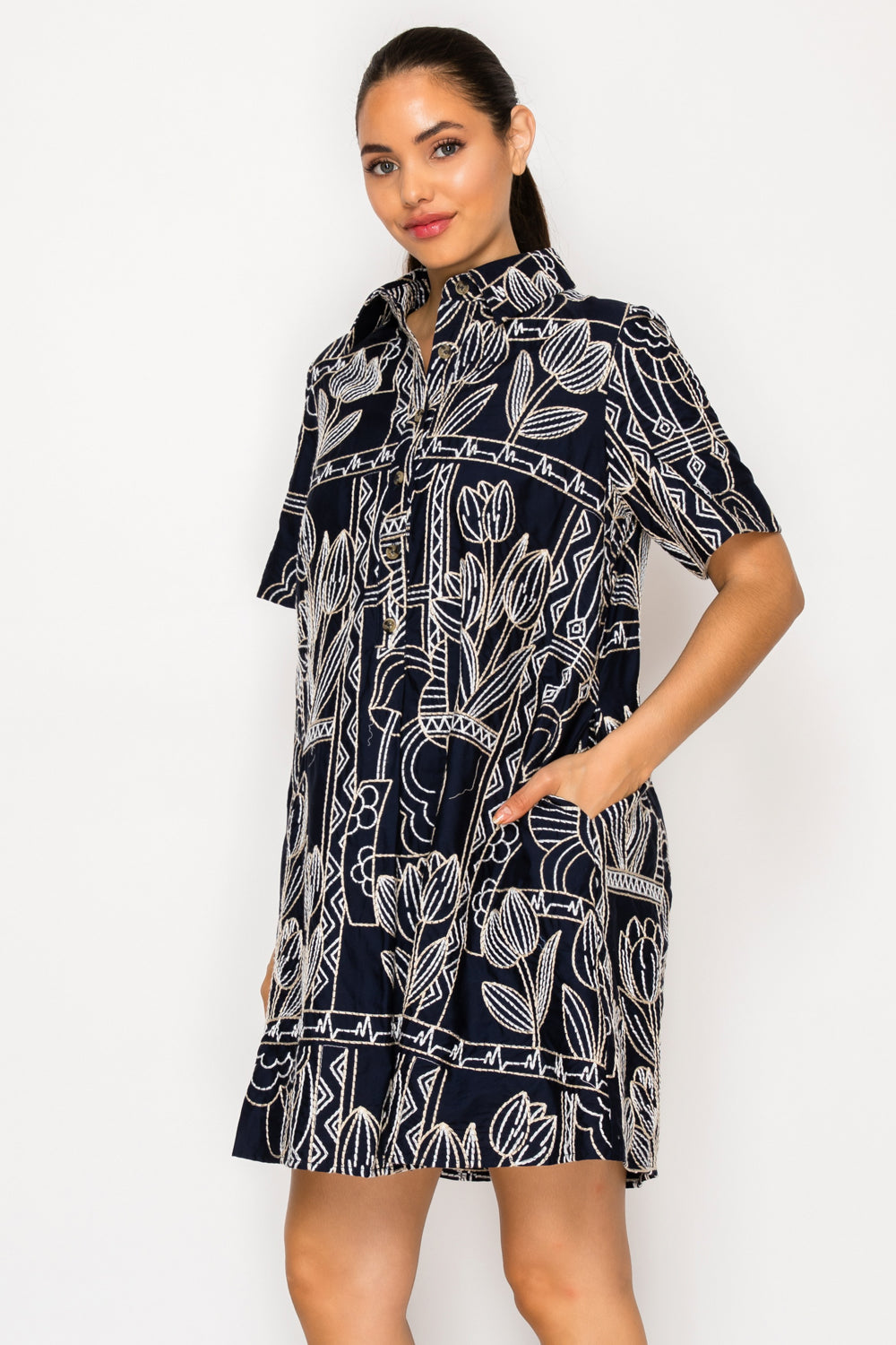 Model wearing the Selene's Stitch Shirt Dress, a navy blue shift dress featuring an intricate cream embroidery-style print, a pointed collar, and short sleeves.