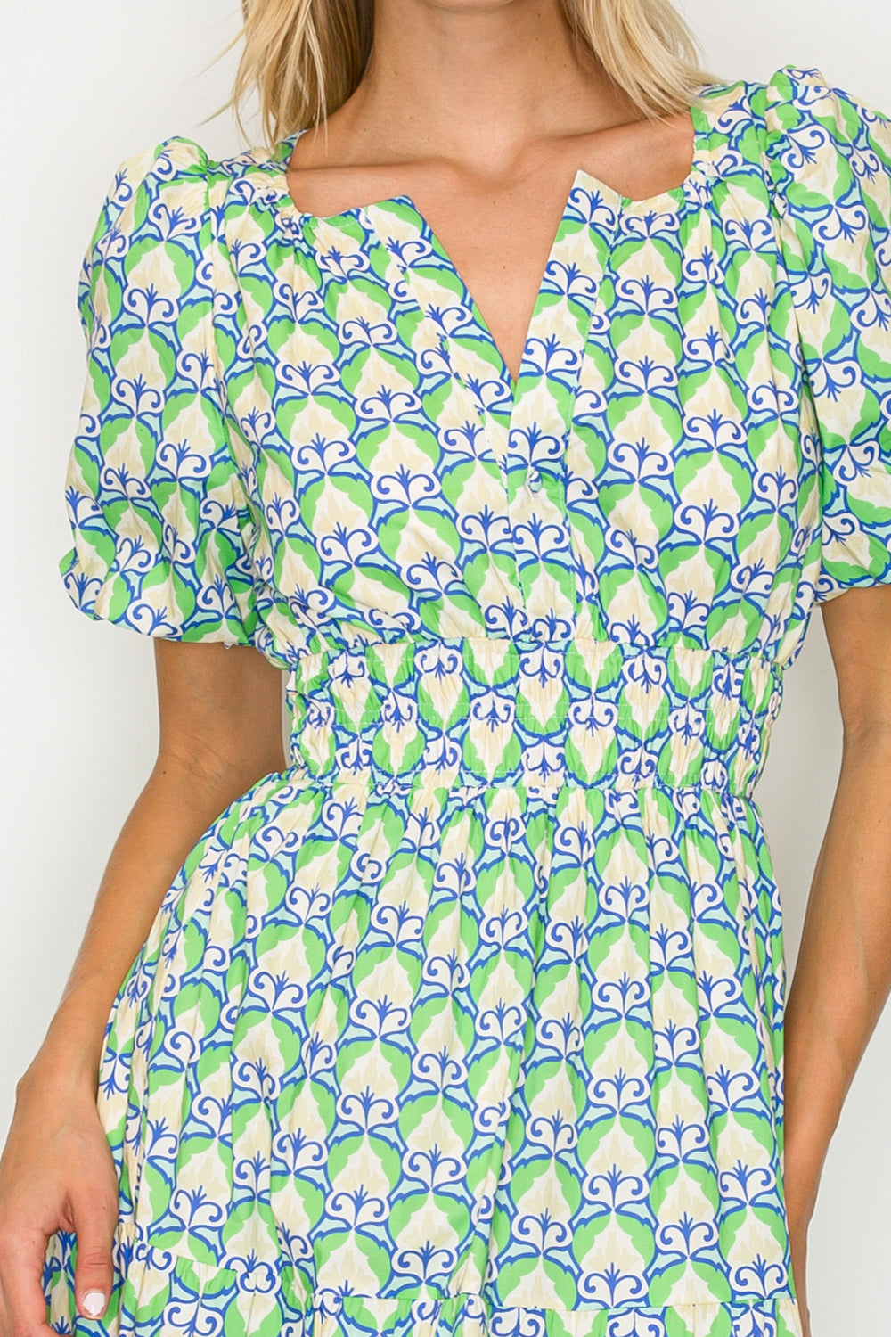 Woman wearing a dress with a green and blue floral pattern on a plain background