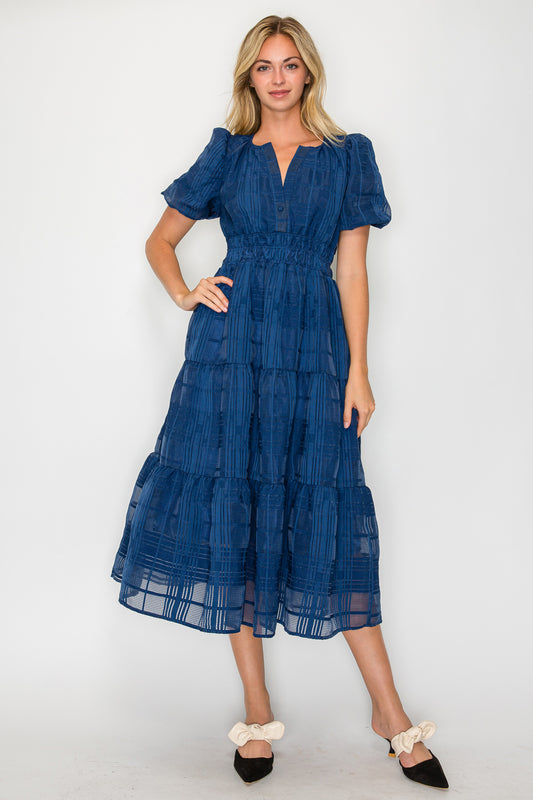 Model wearing the Windowpane Jacquard Puff Sleeve Midi Dress, a navy blue dress with a smocked waist, puff sleeves, and a tiered midi skirt.