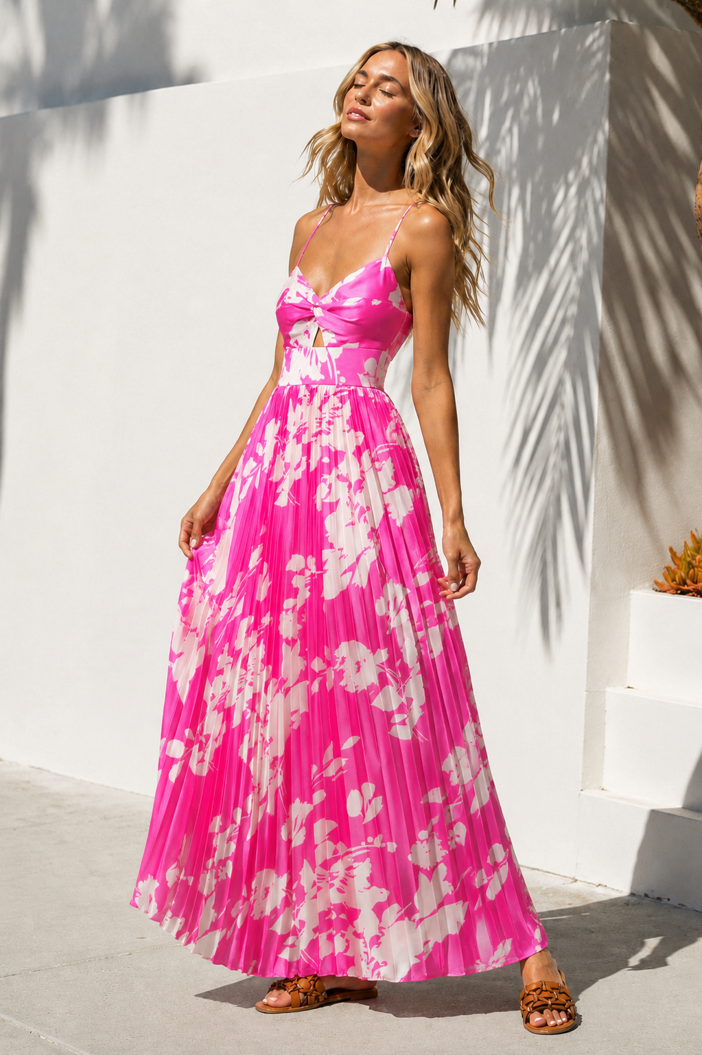 Woman wearing a pink floral dress standing against a white wall.