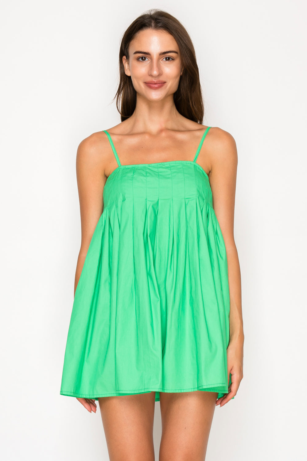 Model wearing the Green Poplin Mini Dress, a vibrant green baby-doll style mini dress with a pleated bodice and thin adjustable straps.
