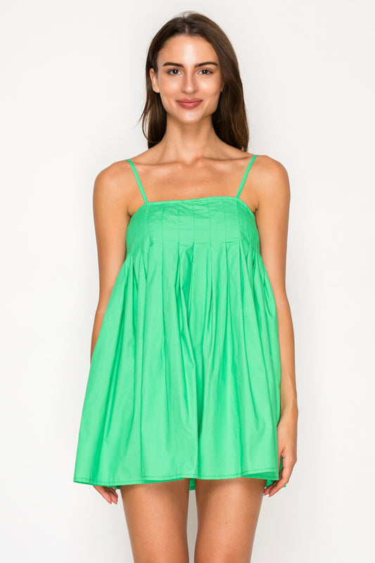 Model wearing the Green Poplin Mini Dress, a vibrant green baby-doll style mini dress with a pleated bodice and thin adjustable straps.