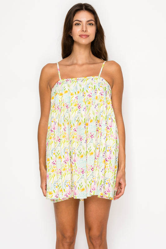 Model wearing the Sirena Garden Mini Dress, a white baby-doll style mini dress with a colorful dainty floral print and thin adjustable straps.