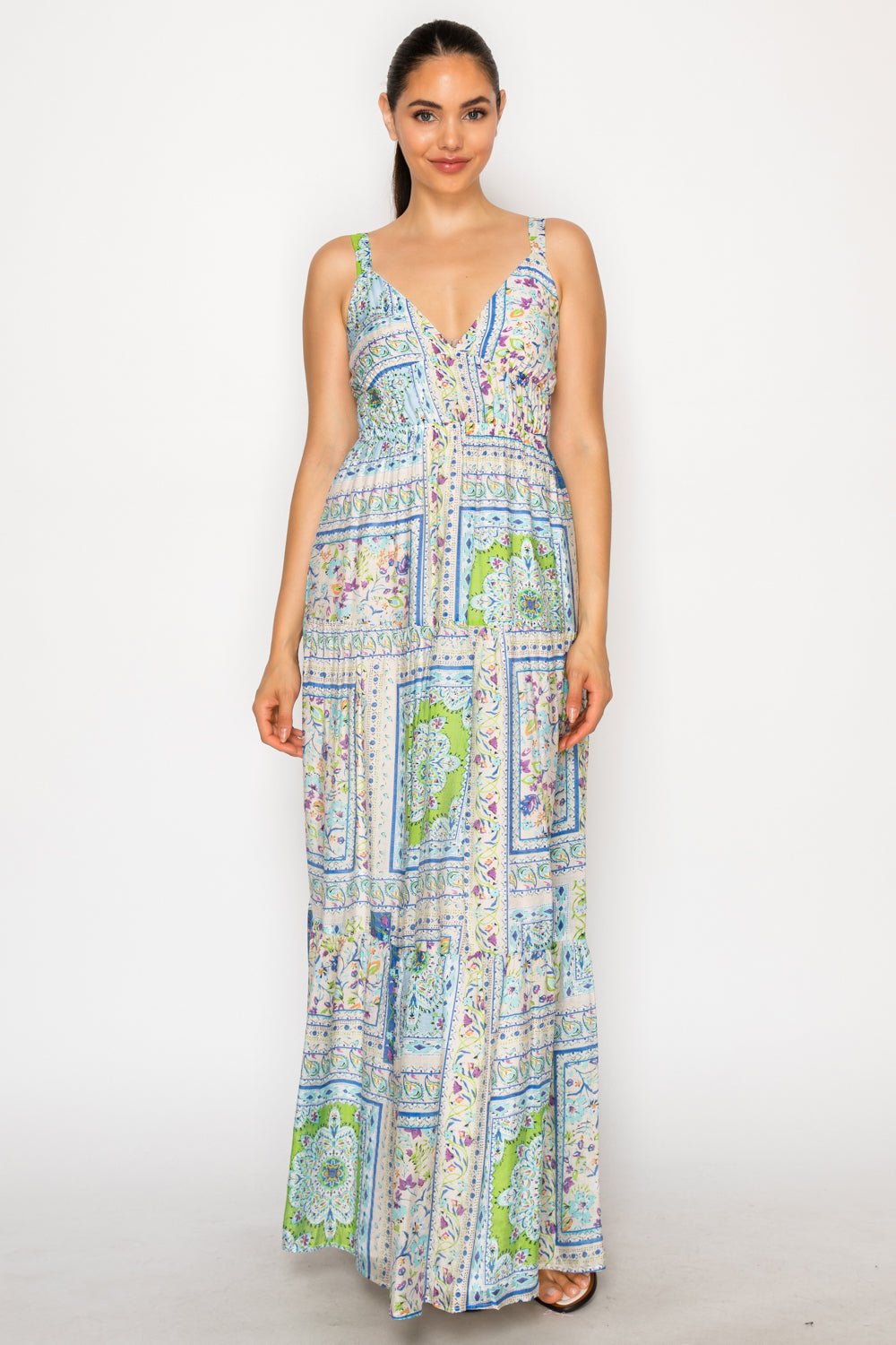 Flat lay of the Helenic Tapestry Maxi Dress, a blue, green, and lavender patchwork print tiered maxi dress with a smocked waist on a white stone background with a straw hat.