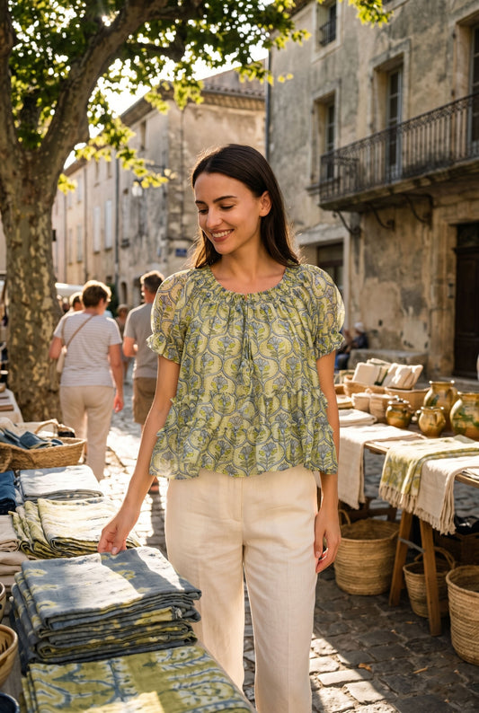 Woman in a green patterned blouse standing in an outdoor market setting.