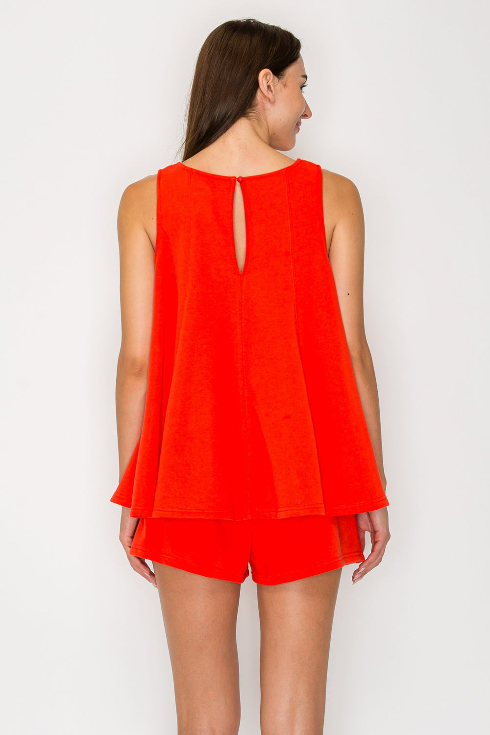 Woman wearing a bright orange sleeveless top and shorts set on a white background
