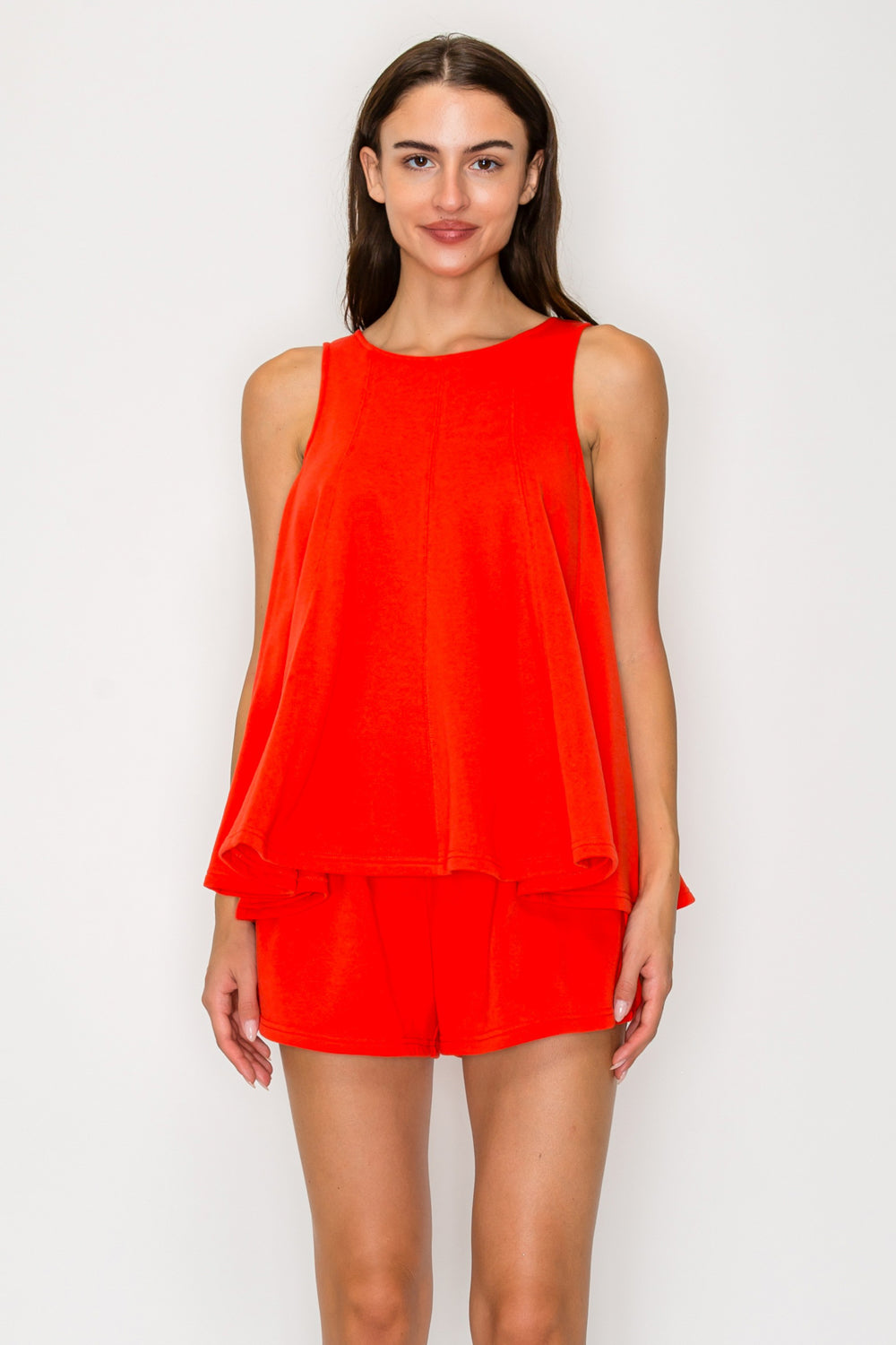 Woman wearing a bright orange sleeveless top against a white background